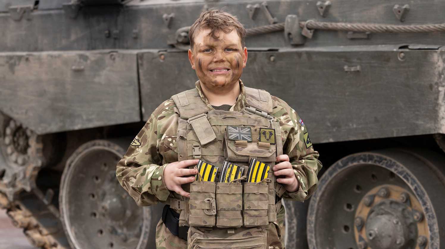 Noah in full army camo gear and facepaint smiles at the camera