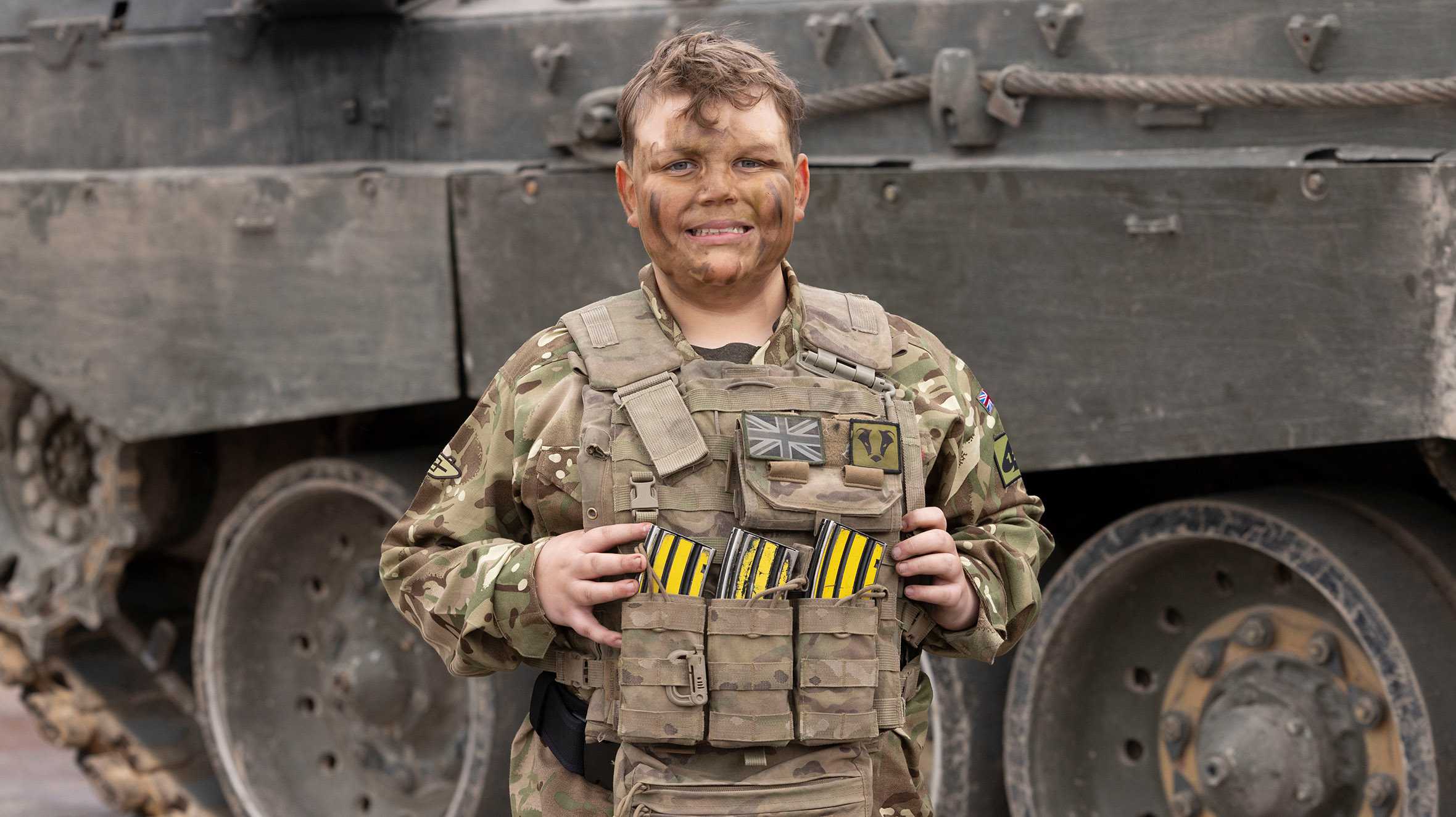 Noah in full army camo gear and facepaint smiles at the camera