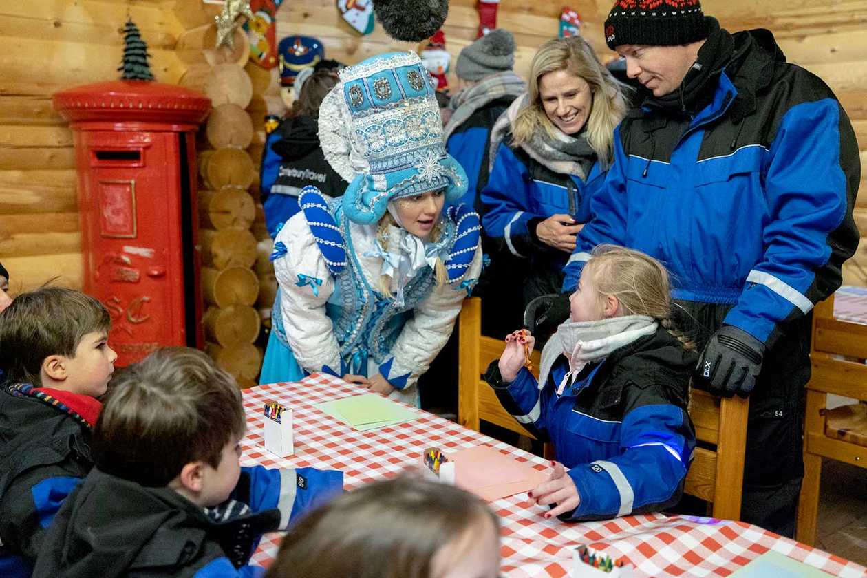 Alice sat at a table with other wish children, chatting to one of Santa's helpers as she writes a letter to Santa.