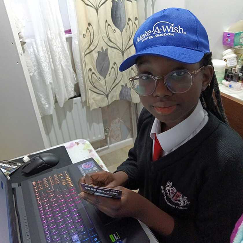Benedicta, wearing a Make-A-Wish hat sits in her room with her new laptop