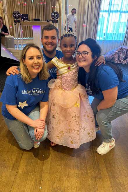 Avia, in her pink princess outfit puts her arm around Make-A-Wish volunteers Ellie, Sean and Abbie