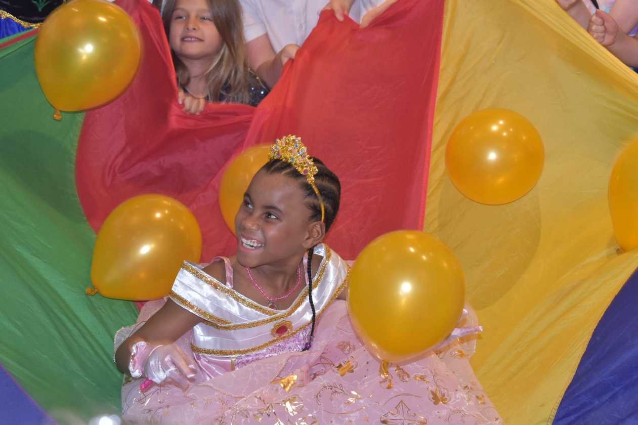 Avia plays with balloons in a multi-coloured flag held by party guests
