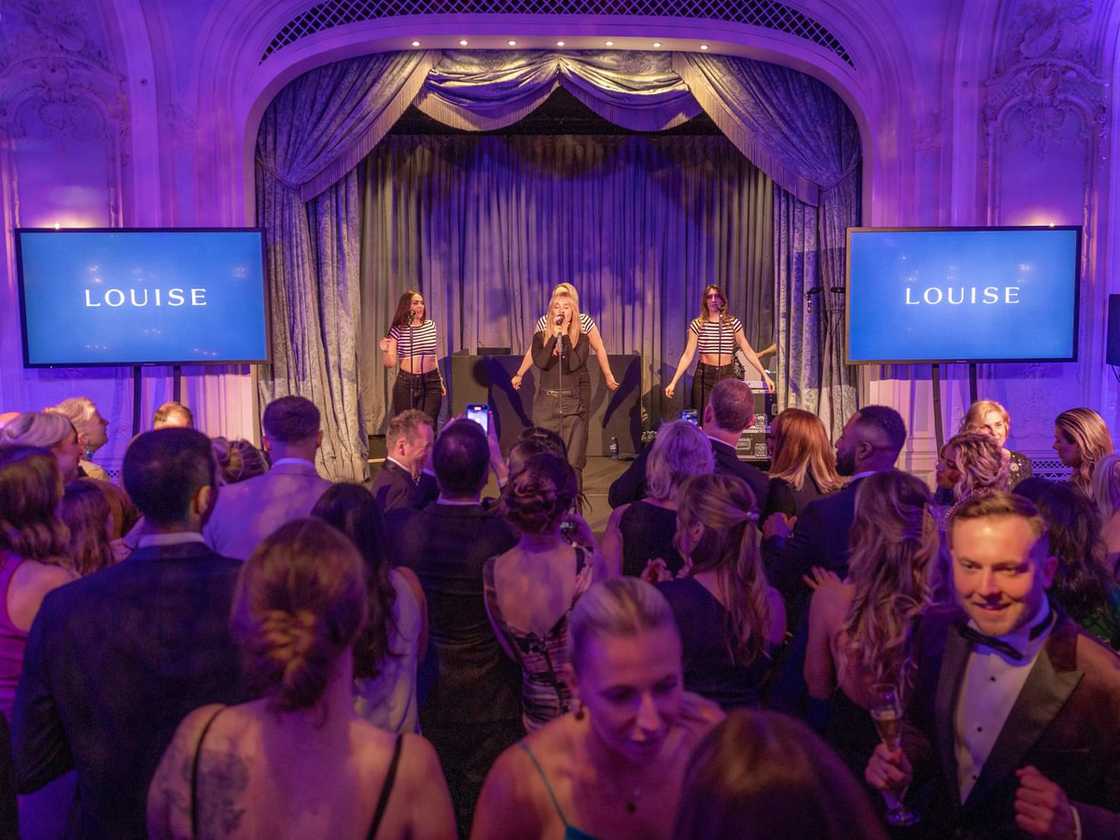 Louise Redknapp performs on stage alongside three backing singers at A Night of Wishes, with a large crowd dancing in front of her.